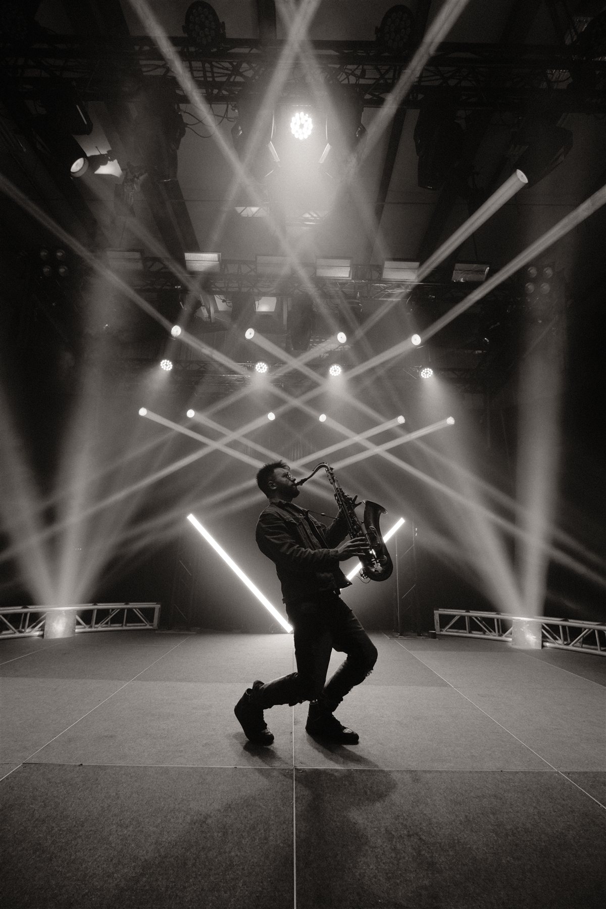 Black and white photo of Lucas playing saxophone mid-motion, surrounded by crossing stage lights