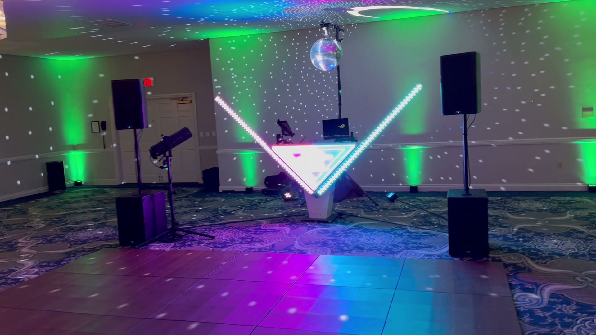 The full DJ booth, disco ball, and lighting rig set up and lit before a reception